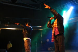 Two members of rap group Coast Contra standing on stage. Their arms are extended out, hyping up the crowd!